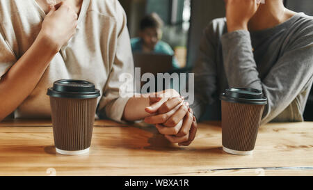 7/8-Porträt von zwei jungen Frauen, die sich in einander die Hände, wie sie in der Cafeteria genießen eine Tasse Kaffee sitzen. Horizontale erschossen. Ansicht von vorn Stockfoto