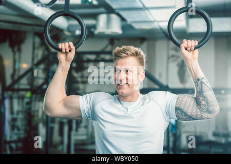 Hübscher junger Mann mit starken Armen hängend an Gymnastik Ringe an der Turnhalle Stockfoto