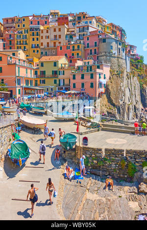 Manarola und Riomaggiore, Italien - Juli 2, 2019: Farbenfrohe Gebäude und Waterfront mit wandern Menschen in Manarola Stadt auf sonnigen Sommertag, Cinque Terre Stockfoto