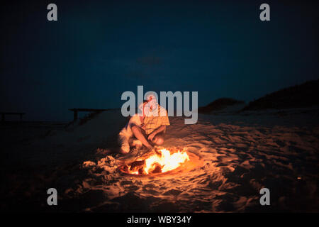 Glückliches junges Paar kuscheln zusammen und bis auf die Sterne neben einem romantisch leuchtenden Lagerfeuer am Strand Blick bei Nacht. Stockfoto