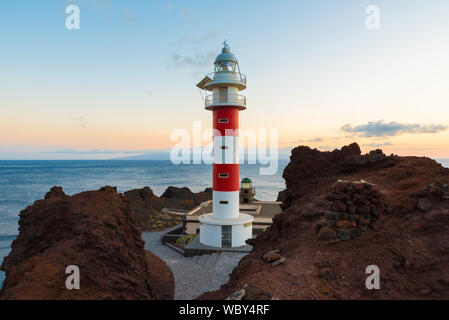 Rot-weiße Leuchtturm von Punta de Teno Teneriffa Kanarische Inseln von Felsen und mit einem wunderschönen Sonnenuntergang im Hintergrund umgeben Stockfoto