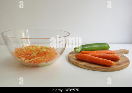 Karotten und Kürbis auf dem hölzernen Schneidebrett. Geriebenen Gemüse in transparenten Schüssel Stockfoto