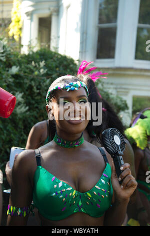 Notting Hill Carnival, 26. August 2019. Eine Feder kostümierte Tänzer kühlt sich ab mit einem batteriebetriebenen Ventilator Stockfoto