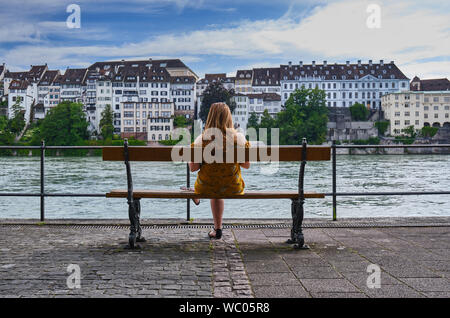 Ansicht der Rückseite Frau sitzt auf der Bank durch den Fluss in der Stadt Stockfoto