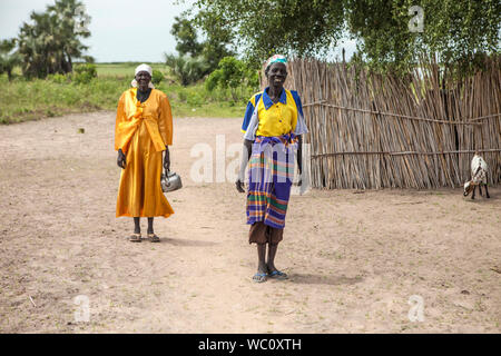 PANWELL, SOUTH SUDAN - NOVEMBER 2, 2013: Nicht identifizierte Frauen in bunten Kleid über ihr Geschäft gehen, in einem kleinen Dorf im Süden des Sudan Stockfoto