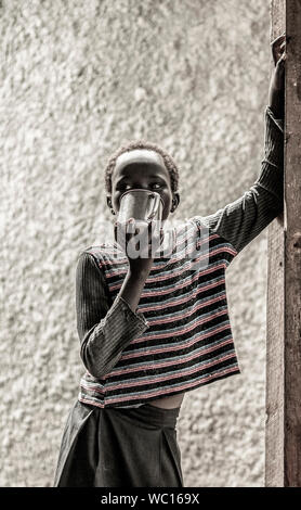 BOR, SOUTH SUDAN - NOVEMBER 4, 2013: Ein unbekannter Süden sudanesische Mädchen Getränke aus einem Tin Cup in Bor, South Sudan Stockfoto