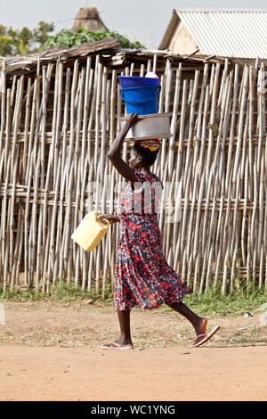 TORIT, SOUTH SUDAN - 21. FEBRUAR 2013: Unbekannter Süden sudanesische Frau trägt mehrere Elemente auf ihren Kopf in das Dorf von Torit Stockfoto