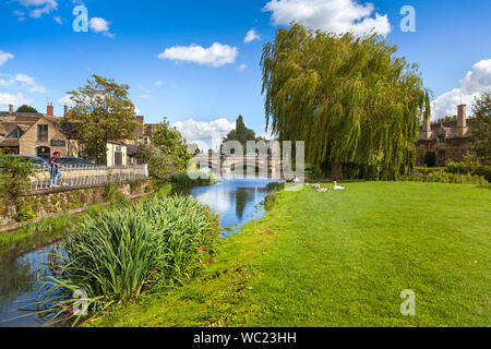 Der Fluss Welland an den Wiesen von der Stadt Brücke, in Stamford, Lincs. UK, helle Sonne mit zwei Touristen genießen die Aussicht Stockfoto