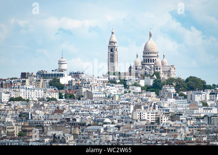 Aussicht auf die Basilika Sacré-coeur an der Spitze des Montmartre in Paris, Frankreich, an einem hellen bewölkten Tag, mit Gebäuden im Vordergrund. Stockfoto