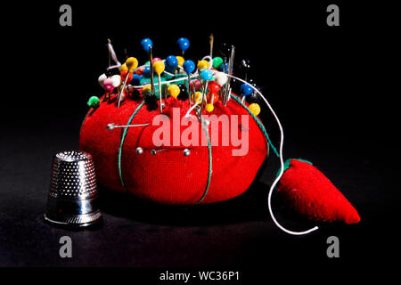 Nahaufnahme von nähen Werkzeuge. Red Pin Kissen mit vielen bunten stick Pins und Nadeln. Kurze Stücke. Metall Fingerhut. Alle auf schwarzem Hintergrund Stockfoto