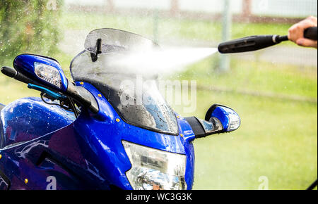 Nahaufnahme der Verwendung von Druckwaschanlage zum Reinigen des Motorrads im Garten, grünem Gras im Hintergrund, Sommertag. Stockfoto