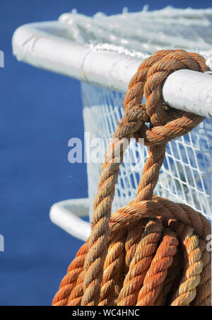 Orange Seil mit einem marine Knoten zu einem Handlauf eines Schiffes gebunden. Das blaue Meer im Hintergrund Stockfoto