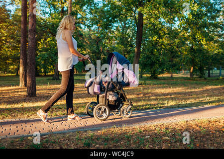 Junge Mutter Walking im Sommer Park mit Kinderwagen. Frau verbringt Zeit mit Ihrem Kind draußen bei Sonnenuntergang Stockfoto