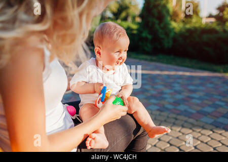 Baby Mädchen mit Spielzeug spielen Sitzen auf den Knien ihrer Mutter im Sommer Park. Familie Spaß im Freien spielen. Stockfoto