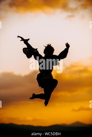 Portrait einer jungen Frau, die gerne tanzen und springen in die Luft am Sonnenuntergang Stockfoto