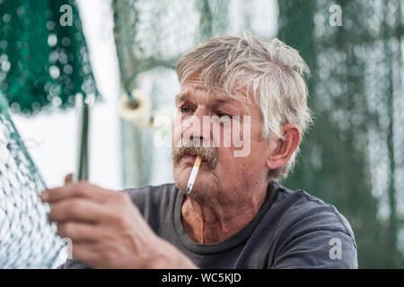 Verwitterte fisherman mends Netze auf einem Fischerboot Stockfoto