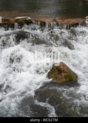 In der Nähe von white water Stolpern über eine braune stein Wand bei Giant Springs, in der Nähe von Great Falls Montana. Einen bemoosten Felsen im Vordergrund. Stockfoto