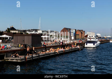 Kopenhagener und Touristen an der hölzernen Pier in Ofelia Platz in der Nähe des Royal Play House und die historische Nyhavn in Kopenhagen, Dänemark. Das Wasser in den Hafen von Kopenhagen ist so sauber, dass es sicher ist, ein erfrischendes Bad zu nehmen. Im Jahr 2018 überstieg in Kopenhagen der CNN-Liste für "besten Städte für Schwimmen". Stockfoto