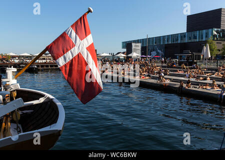 Kopenhagener und Touristen an der hölzernen Pier in Ofelia Platz in der Nähe des Royal Play House (R) und die historische Nyhavn in Kopenhagen, Dänemark. Das Wasser in den Hafen von Kopenhagen ist so sauber, dass es sicher ist, ein erfrischendes Bad zu nehmen. Im Jahr 2018 überstieg in Kopenhagen der CNN-Liste für "besten Städte für Schwimmen". Stockfoto