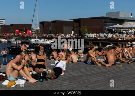 Kopenhagener und Touristen an der hölzernen Pier in Ofelia Platz in der Nähe des Royal Play House (R) und die historische Nyhavn in Kopenhagen, Dänemark. Das Wasser in den Hafen von Kopenhagen ist so sauber, dass es sicher ist, ein erfrischendes Bad zu nehmen. Im Jahr 2018 überstieg in Kopenhagen der CNN-Liste für "besten Städte für Schwimmen". Stockfoto