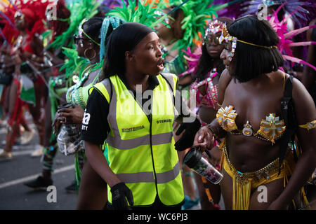 Synterna Sicherheit Steward im Gespräch mit dem Karneval am Notting Hill Carnival durchgeführt. Andere Darsteller im Hintergrund Stockfoto