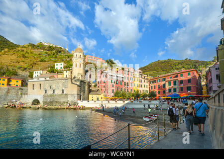 Der Hafen von Vernazza, Cinque Terre Italien mit Kinder spielen am Strand, Touristen, die Stadt und die Kirche von Santa Margherita in der Sonne Stockfoto