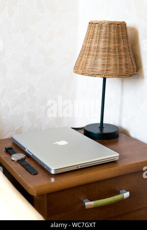 Kedainiai, Litauen - 25. August 2019: Nachttischlampe, Macbook Pro und Armbanduhr auf dem Nachttisch Tisch im Schlafzimmer. Stockfoto