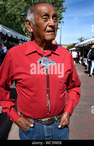 Eine Native American (Navajo) Schmuck Künstler das Tragen einer Seiner bolo Ties steht neben seinem Stand auf der Santa Fe indischen Markt in Santa Fe, New Mexico. Stockfoto