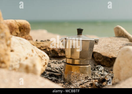 Kaffee am Lagerfeuer am Strand mit dem Meer im Hintergrund. Stockfoto