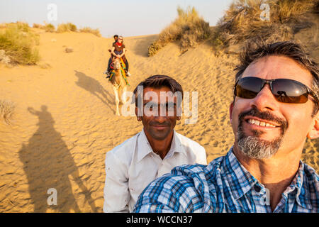 Ein kaukasischer Tourist auf einem Kamel Trek dauert eine selfie von sich selbst und seinem Fahrer sowie seine Frau auf ihrem Kamel mit ihrem Fahrer im Hintergrund. Stockfoto