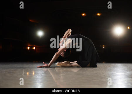 Ballerina in einen schwarzen Anzug ist das Springen auf einem schwarzen Hintergrund in Szene. Stockfoto