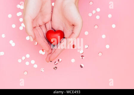 Woman's Hände mit Maniküre halten roten Herzen auf rosa Hintergrund mit glitzert. Festliche Konzept. Stockfoto