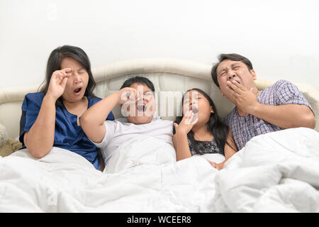 Im Schoß der Familie Schläfrigkeit während das Aufwachen in den frühen Morgenstunden. Vater und Mutter mit Kindern Gähnen und Strecken im Bett, Bettwäsche, Slee Stockfoto