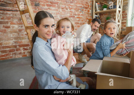 Das neue Leben. Nach zog die Familie in ein neues Haus oder Wohnung. Ehepartner und Kinder glücklich und zuversichtlich. Verschieben, Beziehungen, Lifestyle Konzept. Auspacken der Kartons mit ihren Sachen, die gemeinsam spielen. Stockfoto
