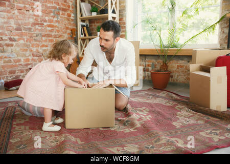 Das neue Leben. Junge Vater und seiner Tochter in ein neues Haus gezogen oder Apartment. Glücklich und zuversichtlich. Verschieben, Beziehungen, Lifestyle Konzept. Gemeinsam Spielen, Auspacken der Kartons und Laughting. Stockfoto