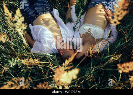 Glückliches Paar mit schwangeren Frau liegt auf der Wiese unter Gras bei einem Spaziergang. Ansicht von oben. Stockfoto