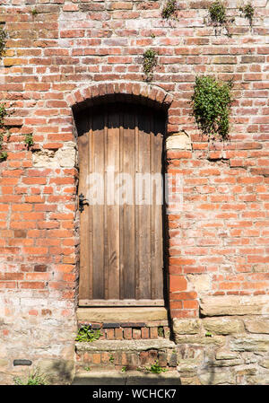 Alte Holztür in Red brick wall, Silk Mill Lane, Ludlow GROSSBRITANNIEN. April 2019. Stockfoto