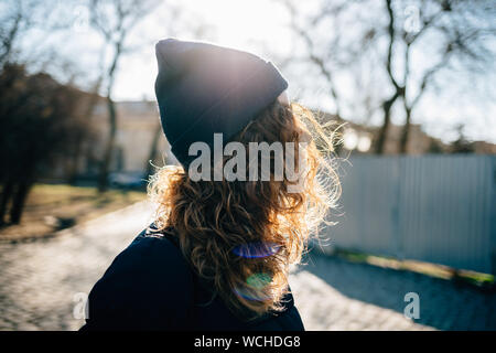 Close-up unkenntlich junge Frau mit lockigem Haar in einer Beanie-mütze außerhalb von Winter Tag, Sonne von hinten. Stockfoto