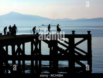 Die halb verfallenen Pier in der kleinen Ortschaft Portencross auf dem Clyde Küste, ist ein für die Menschen, die Fisch aus, was der Struktur links ist. Dies ist eine ästhetische und künstlerische, Foto von der Pier mit den Fischern in Silhouette geworfen zusammen mit der Struktur. Ein riesiger Tanker gesehen werden kann, die sich durch den Firth of Clyde in Schottland. Alan Wylie/ALAMY © Stockfoto