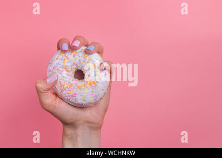 Woman's Hand mit Maniküre Holding einen Krapfen auf rosa Hintergrund Stockfoto