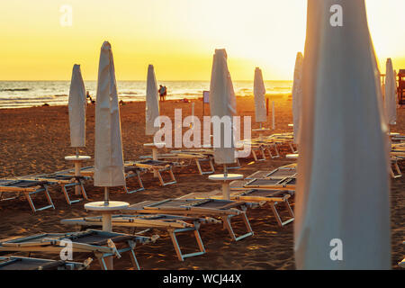 Gefaltete Liegestühle und Sonnenschirme auf leeren Strand am Abend Stockfoto