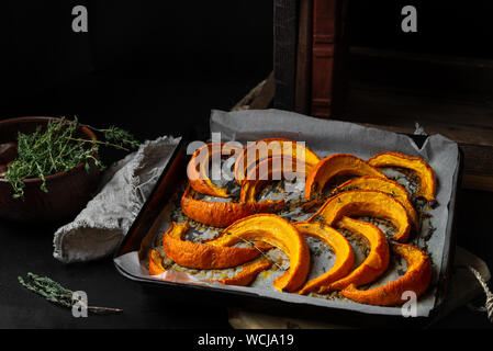 Gebackene geschnittenen Kürbis Stücke auf Backblech, frischem Thymian auf dunklem Hintergrund als Zutaten für einen Fall Gericht. Bild horizontal. Stockfoto