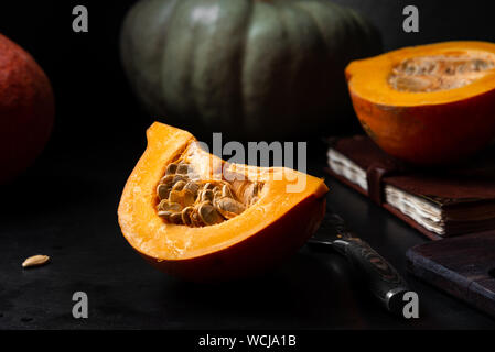 Stillleben mit Vielzahl von Herbst Kürbisse auf einem schwarzen Hintergrund, ganz und halbiert. Bild horizontal, Detailansicht. Stockfoto