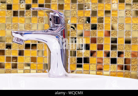 Wasserversorgung Wasserhahn Mischpult auf dem Hintergrund der gelben keramische Mosaikfliesen. Stockfoto