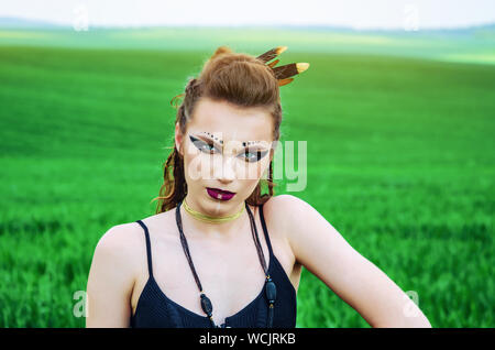 Aggressive Make-up Girl, Schlacht Gemälde des Gesicht von Amazon in einem Feld inmitten grüner Weizen. Feminismus, der Unabhängigkeit, der Stamm. Stockfoto