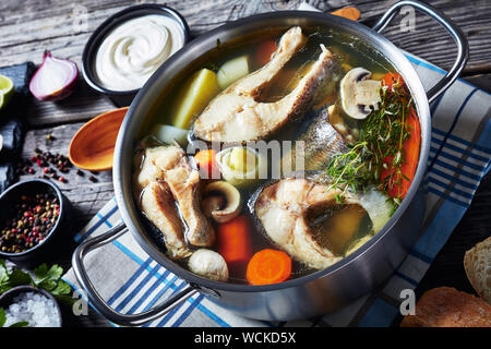 Nahaufnahme der pikanten Forelle Fischsuppe mit Gemüse und Pilzen in einem Topf auf einem hölzernen rustikalen Tisch mit Zutaten, horizontale Ansicht von abov Stockfoto