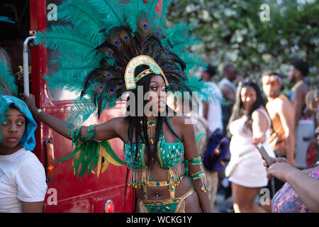 Performerin gekleidet in Pfauenfedern auf einem roten London Bus an der Notting Hill Carnival, größte Karneval in Europa Holding. Sie suchen Stockfoto