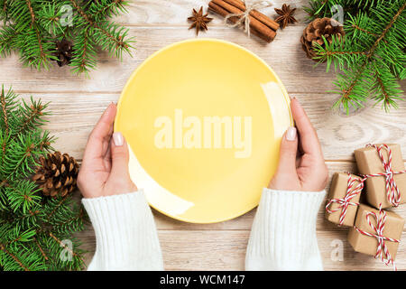 Mädchen Hand halten Leere gelbe Platte auf Holz- Hintergrund mit Weihnachtsdekoration. Neues Jahr Konzept Top anzeigen. Stockfoto