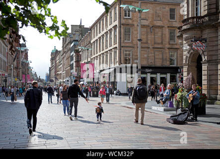 Buchanan Street Glasgow, Schottland, Großbritannien. 28 Aug, 2019. Käufer und Besucher wandern entlang in die dunstige Sonnenschein durch die pedestriansed Buchanan Street in Glasgow. Der Donald Dewar statue stolz an der Oberseite der Straße steht, der erste Minister von Schottland und ein Fürsprecher der Scottish Devolution, würde man mich fragen, was seine Gedanken würden zur heutigen breaking news, dass der britische Premierminister Boris Johnson die Königin gebeten hat das britische Parlament ab Mitte auszusetzen - September. Stockfoto