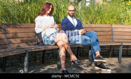 Das glückliche Paar sitzt auf der Bank im Park in der Nähe der jeweils anderen, schönen Sommertag. Konzepte der Sommer, Liebe, Zweisamkeit, Beziehung Stockfoto